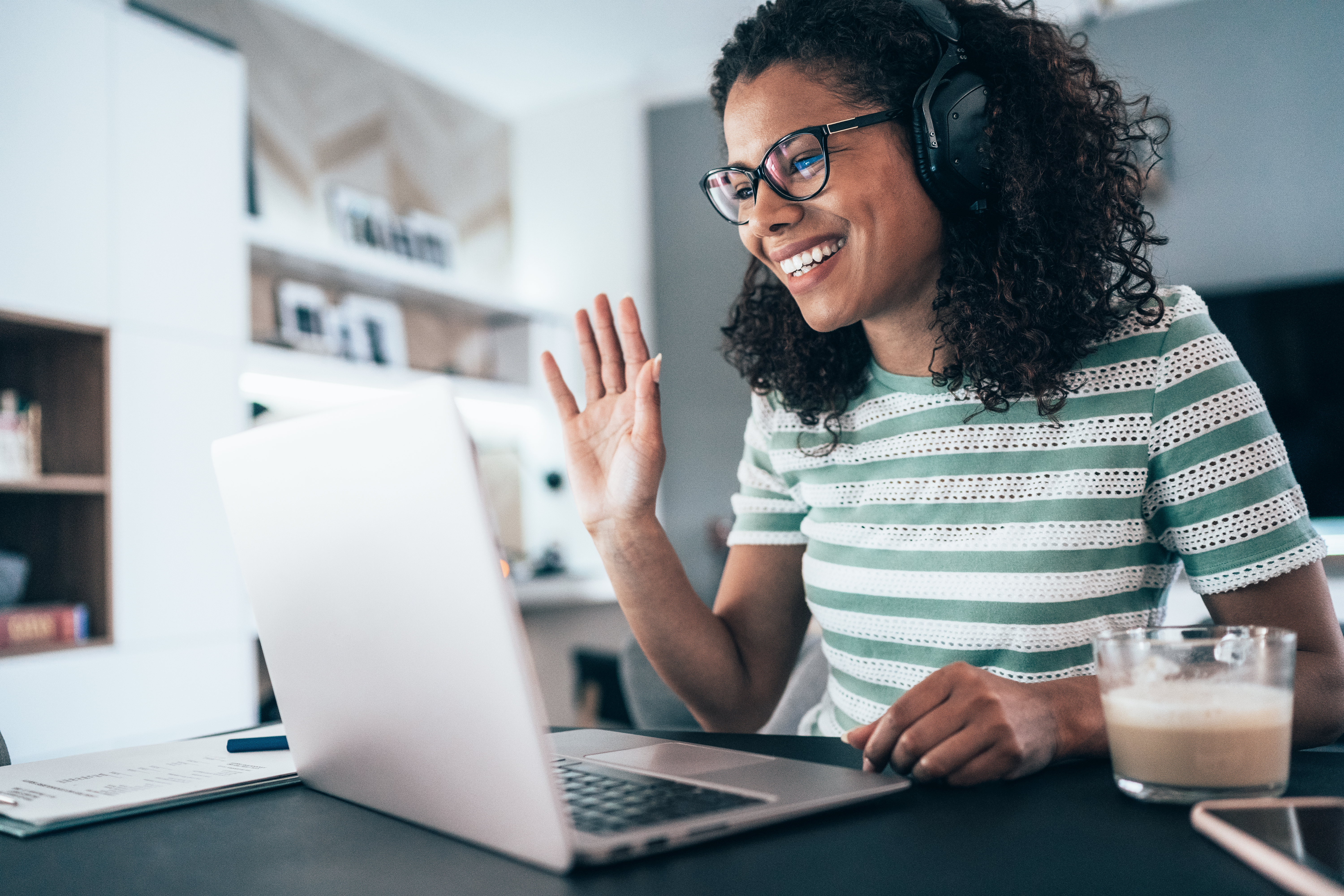 Mujer usando auriculares. Está sonriendo y saludando a la computadora.